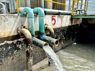 Industrial wastewater pipes discharging liquid into a treatment pond. Rusted pipes and algae...