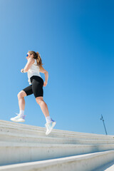 Fitness enthusiast strides confidently up outdoor stairs under a clear blue sky