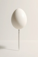 Delicate white egg perfectly balanced on the tip of a vertical needle, symbolizing precision and fragility