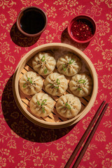 Traditional steamed dumplings in bamboo basket served with soy sauce and chili on red floral tablecloth