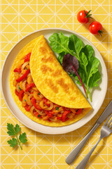 Fluffy omelette filled with saut?ed bell peppers and onions served with fresh greens on a plate
