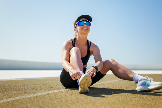 Cheerful athlete ties shoes before running on the track under clear blue sky