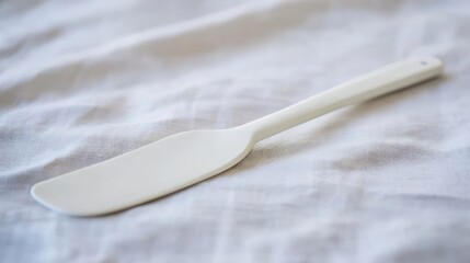 Minimalist Still Life: An Unused White Spatula Resting Gently on Wrinkled White Linen Fabric, Highlighting Purity and Simplicity in Kitchenware Photography