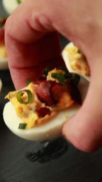 vertical stock video showing close up of delicious deviled eggs topped with crispy bacon