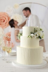 Happy married couple together indoors, focus on wedding cake and glasses of champagne on table