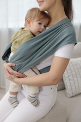 Fototapeta premium Mother holding her child in sling (baby carrier) at home, closeup