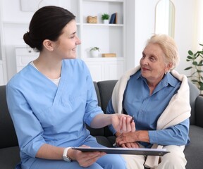 Nurse with clipboard examining senior woman indoors. Home health care service
