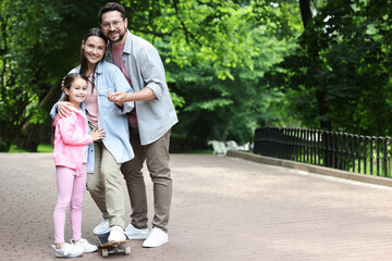 Obraz premium Happy family having fun with skateboard in park. Space for text