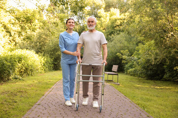 Smiling nurse supporting elderly man who using walking frame outdoors