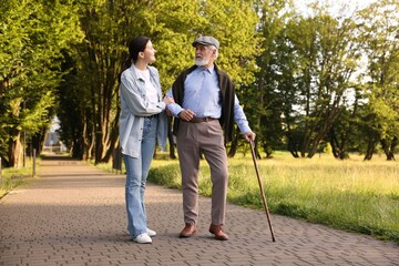 Smiling caregiver supporting elderly man with walking cane outdoors