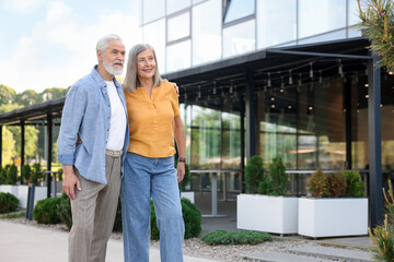 Lovely senior couple walking together near building outdoors, space for text
