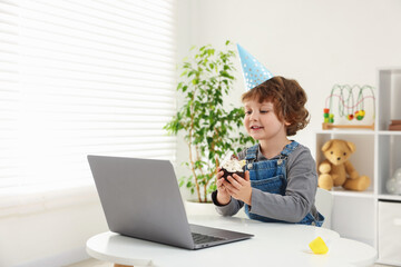 Birthday celebration. Little boy with cupcake having video call via laptop at table indoors. Space...