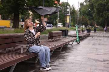 Woman with broken umbrella on bench in park