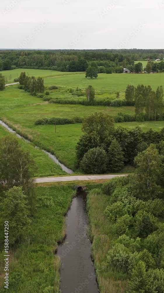 Poster stream flowing between the green fields with trees in summer. - aerial pullback shot