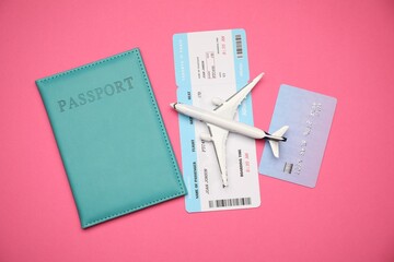 Airplane model, passport, flight ticket and credit card on pink background, flat lay