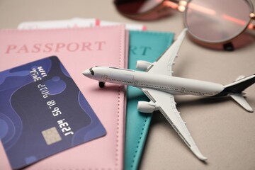 Airplane model, passports, flight tickets, credit card and sunglasses on beige background, closeup