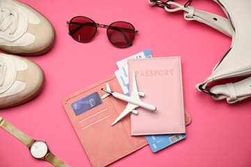 Airplane model, passport, flight tickets, credit card, and accessories on pink background, flat lay