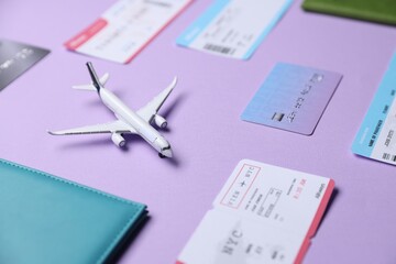 Fototapeta premium Airplane model, passport, credit card and flight tickets on violet background, closeup