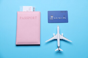 Airplane model, flight ticket, passport and credit card on light blue background, flat lay