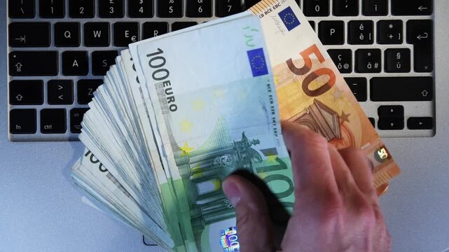 A man withdraws 10,000 euros in 100, 500, 50 eurbills from a laptop keyboard. Concept of earning with internet with online business or network marketing. Trading online. earn money with the internet