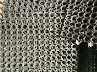 Top view of black industrial rubber floor mats with circular hole pattern. Durable anti-slip...