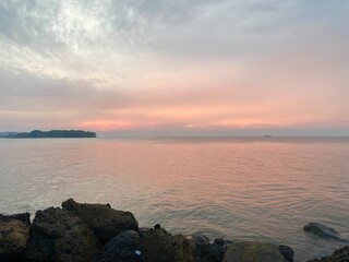 Beautiful sunset over the ocean with calm water and rocks in the foreground. Peaceful coastal landscape with pink and orange sky. Serene evening at the beach for travel and nature background.