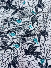 A wrinkled, full-frame tropical textile print featuring stylized black and turquoise leaves on a white background. Fabric texture and summer fashion.