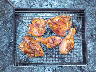 Grilled chicken legs and thighs cooking on barbecue grill over charcoal embers