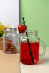 Close-up of a vibrant red strawberry beverage in a mason jar mug with a straw and fresh berry garnish. Refreshing summer cold drink concept.
