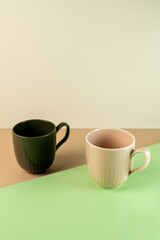 A pair of modern ribbed ceramic mugs, dark green and beige, on a stylish geometric background of pastel colors. Minimalist concept with ample copy space.