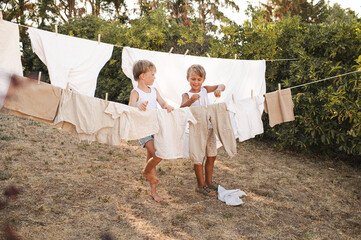 Two boys hanging laundry on an outdoor clothesline using wooden clothespins. Sunny countryside...