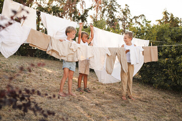 Vintage-style rural scene with young boys hanging laundry outdoors using wooden clothespins....