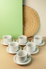 A set of clean, white ceramic coffee or tea cups and saucers arranged on a minimalist two-tone beige and green background with copy space.
