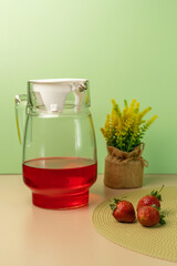 Glass pitcher of red strawberry iced tea or juice with fresh strawberries and yellow Solidago...