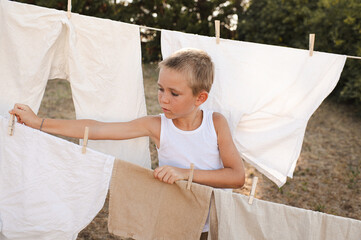 Young boy hanging laundry on outdoor clothesline with wooden clothespins. Sunny countryside...