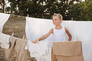 Young boy hanging laundry on outdoor clothesline with wooden clothespins. Sunny countryside...
