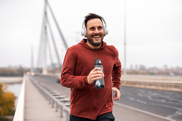 Smiling Man Jogging on Bridge While Listening to Music