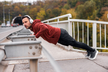 Man Exercising Outdoors with Headphones Performing Push-Ups on Bridge Railing