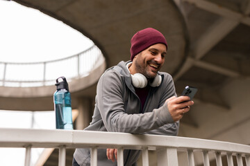 Smiling Man Outdoors Using Smartphone With Headphones and Water Bottle