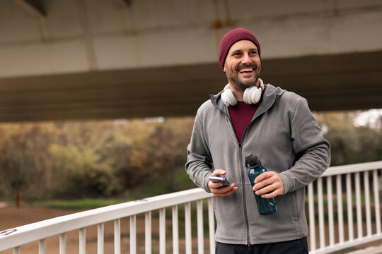 Man Smiling Outdoors Carrying Water Bottle and Phone