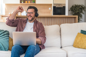 Winner business mindset. Young freelance businessman sitting at home on sofa, working on laptop...