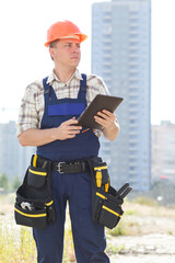 Serious male builder with electronic tablet in hands. Seating is on a new construction site. Male construction engineer with touch pad and checking building, site construction. Get important message