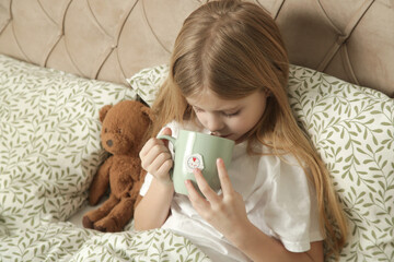 Sick little girl in bed with a cup of tea, cold and flu season, natural herbal remedy	
