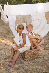 Two boys sitting on a box under clotheslines with freshly washed laundry, enjoying playful summer...