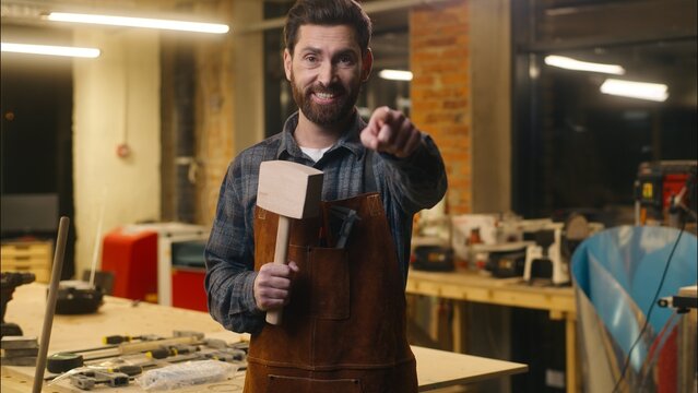 Joyful Caucasian carpenter wood master man wave hand come here gesture in workshop repairman architect recruitment craftsman male builder inviting worker holding wooden hammer guy welcoming sign smile