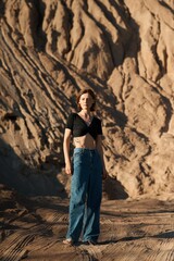 A woman poses in front of a natural rock formation with a relaxed attitude and fashionable style.