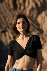 A beautiful woman with short brown hair poses in the sunlight wearing a black top and jeans.