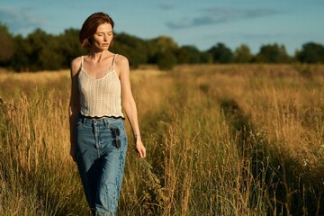 A woman walks through a field of tall grass on a sunny afternoon, enjoying a peaceful day.