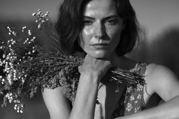A beautiful woman with flowers gazes directly at the viewer in this striking black and white...