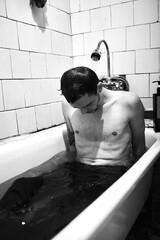 A man in a bathtub, with a pensive expression and water cascading over him.